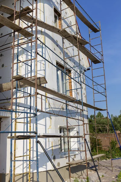 The process of building wall insulation using polystyrene in the open air. Scaffold on house, renovation. House for renovation with the scaffolding for workers on building, close up