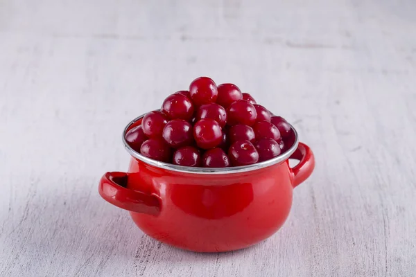 Red cherries in red enamel saucepan on white background, close up