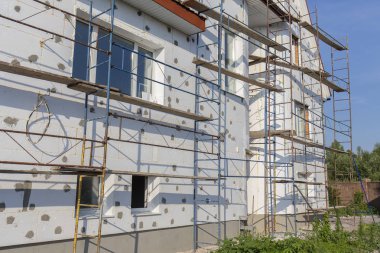 The process of building wall insulation using polystyrene in the open air. Scaffold on house, renovation. House for renovation with the scaffolding for workers on building, close up clipart