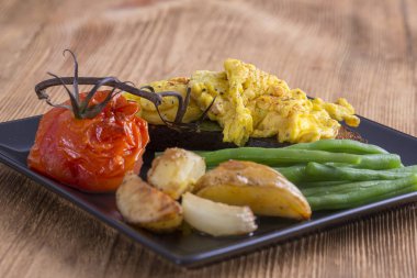 Bir parça kırmızı domates, fasulye, kızarmış patates bir ahşap masa arka plan üzerinde siyah ekmek üzerinde yumurta omlet kapatın. Kahvaltı konsepti