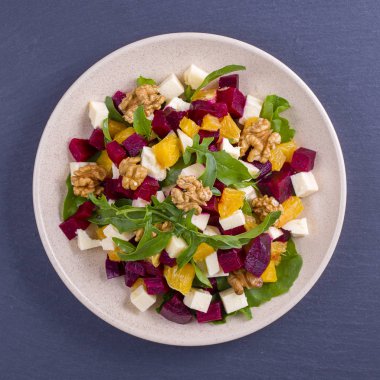 Sağlıklı vejetaryen salatası pancar, yeşil roka, portakal, beyaz tabakta beyaz peynir ve ceviz.
