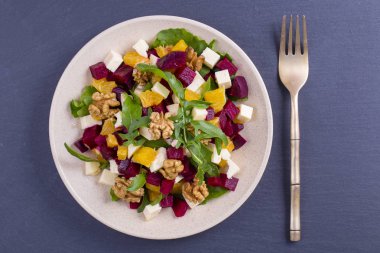 Pancar, yeşil roka, turuncu, beyaz peynir ve ceviz beyaz tabakta salata sağlıklı vejetaryen yakın çekim, görünümü top