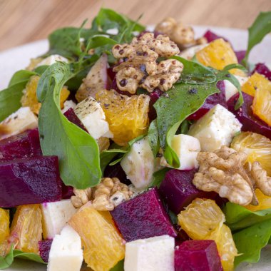 Sağlıklı vejetaryen salatası pancar, yeşil roka, portakal, beyaz tabakta beyaz peynir ve ceviz.