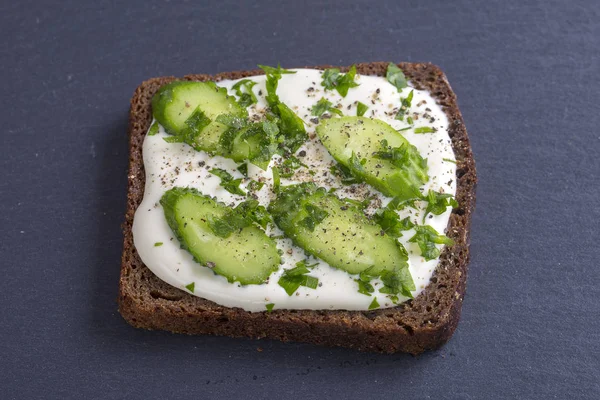 Vegetarian sandwiches with cream cheese, cucumbers and parsley, healthy snack on black slate background, close up