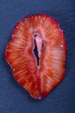 Siyah arka planda kırmızı çilek dilimi, yakın plan, üst manzara. Kırmızı çileği de kadın cinsel organı gibi kes.