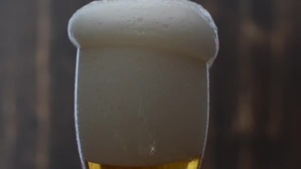 La bière froide et légère se verse du haut dans le verre sur fond de bois foncé, gros plan, macro 