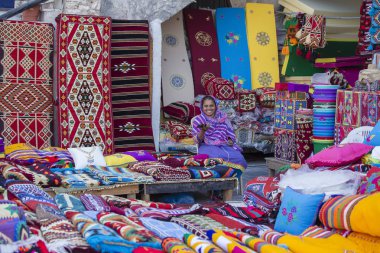 Doha, Katar - 25 Aralık 2017: Multicolour halı, kilim ve diğer öğeleri ile Doha, Souq Waqif pazarı, kadın tüccarı. Doha, Qatar