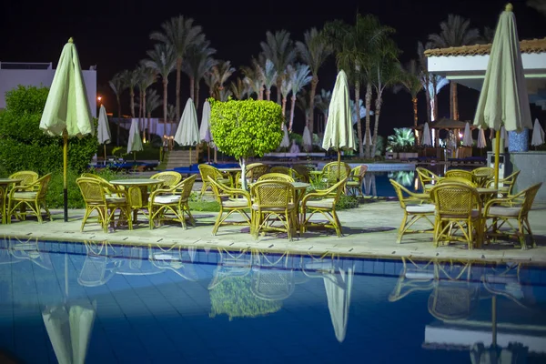 Night view to the swimming pool and palm trees on the beach near the red sea in Sharm El Sheikh, South Sinai, Egypt. Rattan tables and chairs near swimming pool water