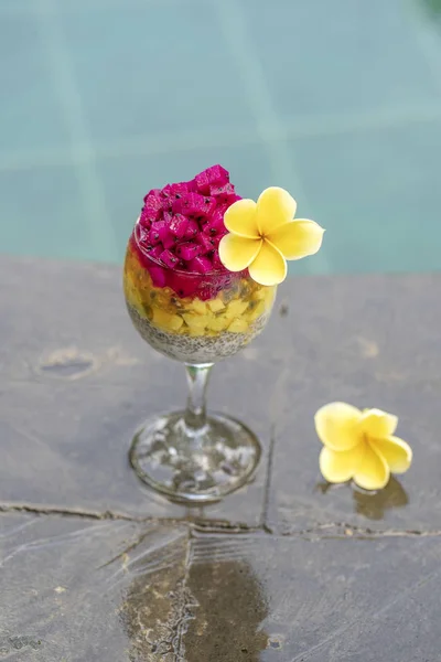 Chia frön pudding med röda drakfrukt, passionsfrukt, mango och avokado i ett glas till frukost på bakgrunden av poolvatten, närbild. Begreppet hälsosam kost. — Stockfoto