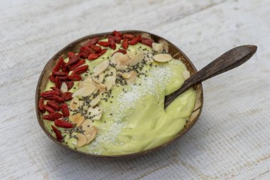 Avokado ile Hindistan cevizi kase yeşil smoothie, kırmızı Goji çilek, badem gevreği, kahvaltı için Hindistan cevizi cips ve Chia tohumları, yakın. Sağlıklı yeme kavramı, Superfood