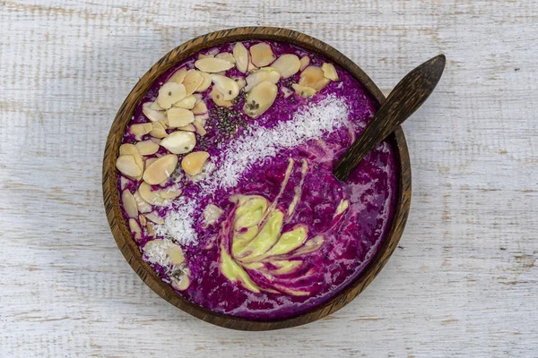 Roter Smoothie in Kokosnussschale mit Drachenfrüchten, Avocado, Mandelflocken, Kokosraspeln und Chiasamen zum Frühstück aus nächster Nähe. das Konzept der gesunden Ernährung, Superfood — Stockfoto