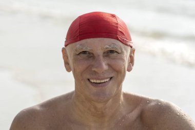 Deniz suyu yakınındaki sahilde kırmızı yüzme şapkalı yaşlı adam