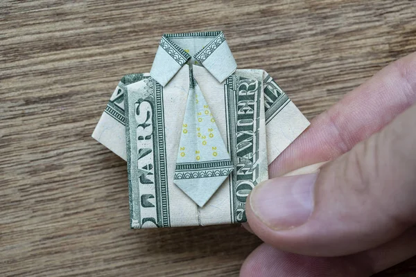 Koszula origami wykonana z banknotu dolara i dłoni na drewnianym tle. Zbliżenie. Koszulka Dollar Bill — Zdjęcie stockowe