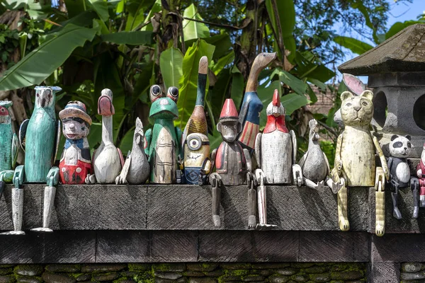 Velhos brinquedos de lembranças de madeira na cerca de pedra perto da loja de bonecas em Ubud, ilha de Bali, Indonésia. Fechar. — Fotografia de Stock