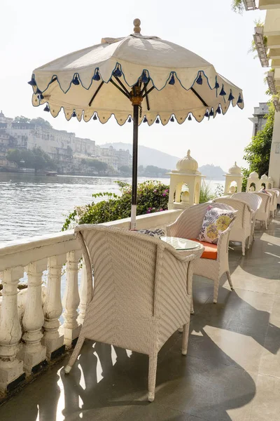 Rattan table and chairs under an umbrella in a street cafe on the shore near the lake in Udaipur, Rajasthan, India.