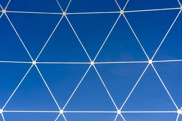 Rejilla de metal blanco en forma de formas geométricas sobre un fondo de cielo azul — Foto de Stock