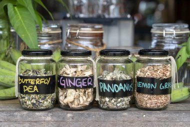 Ahşap arka plan üzerinde cam şişelerde kurutulmuş baharat çeşitleri. Cam kavanozlarda kuru zencefil, pandanus, limon otu ve kelebek bezelye, closeup