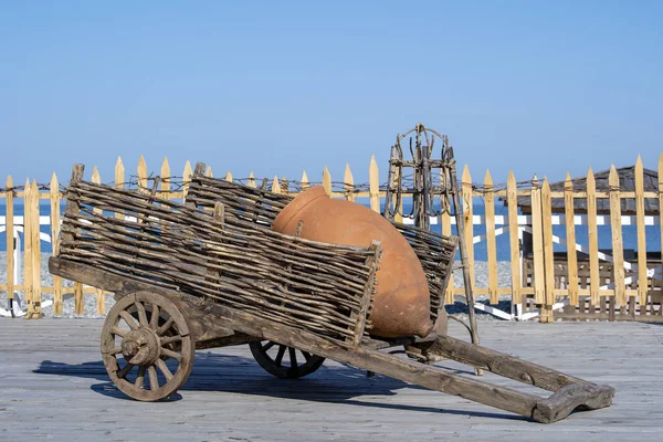 Carrinho de madeira decorativo com jarro de barro fica em uma costa perto da água do mar em Batumi, Geórgia — Fotografia de Stock