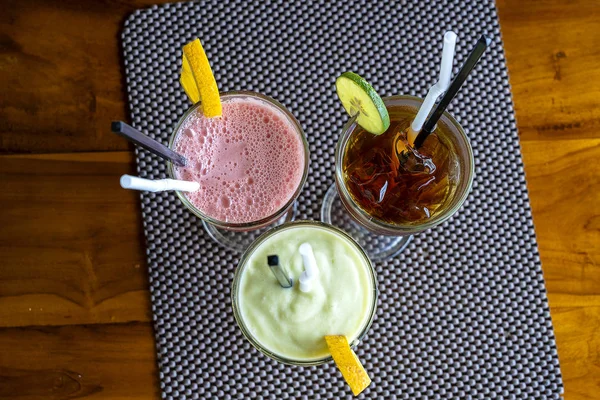 Avocado smoothie, watermelon shake and cold tea in a glass on a wooden table. Tropical drink concept . Top view, closeup