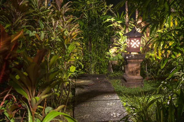 Decorative lamp on the stone pillar next to the path in the tropical garden at night . Island Bali, Indonesia . Nature concept