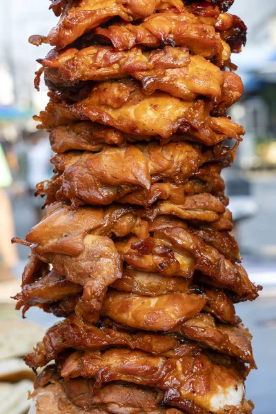 Large pieces of meat on a spit at street food market in Thailand. Crilled skewered chiken meat on spit. Fast food.