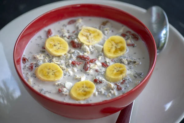 Fresh breakfast of granola, yogurt, nuts, goji berries, chia seeds and banana. Muesli with fruits and berries in red bowl — Stock Photo, Image