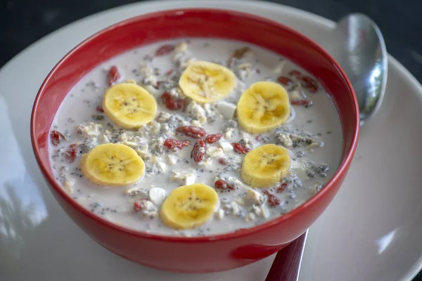 Frisches Frühstück mit Müsli, Joghurt, Nüssen, Goji-Beeren, Chiasamen und Bananen. Müsli mit Früchten und Beeren in roter Schüssel — Stockfoto