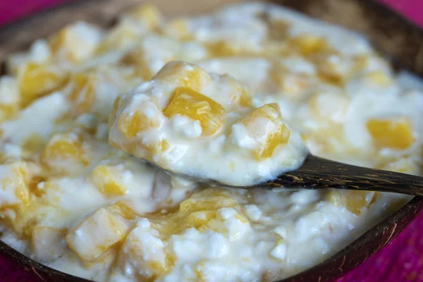 Plátky zralých sladkých žlutých mango ovoce s bílým tvarovým sýrem, medovou a kyselou smetanou v kokosové misce, zaostřená — Stock fotografie