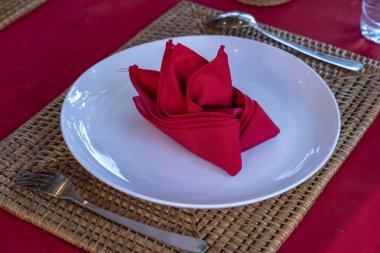 Restoranda çatal, kaşık, beyaz plaka ve kırmızı peçete ile zarif masa ayarı. Düzenlenmiş gümüş ve peçeteler ile güzel yemek masası seti
