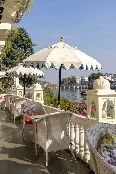 Rattan table and chairs under an umbrella in a street cafe on the shore near the lake in Udaipur, Rajasthan, India.