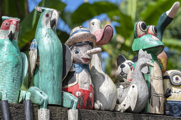 Старые деревянные сувенирные игрушки на каменном заборе возле кукольного магазина в Убуде, остров Бали, Индонезия. Крупный план
