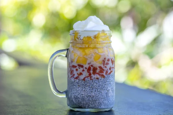 Almond milk chia pudding with fresh yellow mango and red goji berries in a glass jar mug. Vegan raw breakfast. Chia seeds and fresh cut fruits and berries dessert