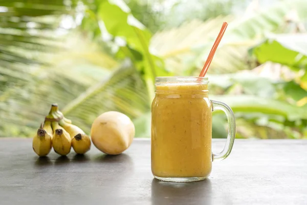 Smoothie com frutas tropicais: manga, banana, abacaxi em um frasco de vidro na mesa de madeira. O conceito de um estilo de vida saudável. Fechar — Fotografia de Stock