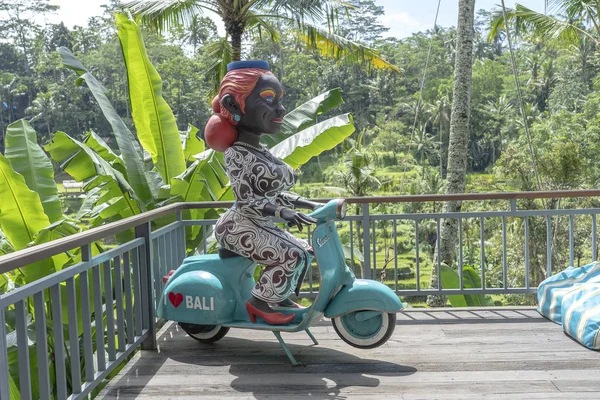 Figura de una mujer de piel oscura sentada en una motocicleta Vespa en una cafetería tropical cerca de terrazas de arroz de Tegallalang en Bali, Indonesia — Foto de Stock