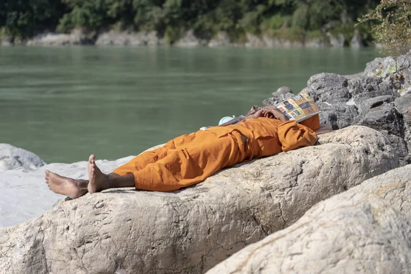 Индуистский садху святой человек, спит на берегу покрыл голову газетой в солнечный день около реки Ганг воды в Ришикеш, Индия, крупным планом — стоковое фото