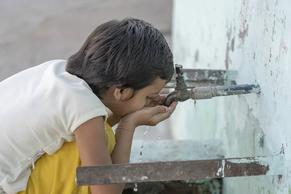 Retrato de la sedienta chica india bebe agua del grifo al aire libre en la calle en Rishikesh, India —  Fotos de Stock