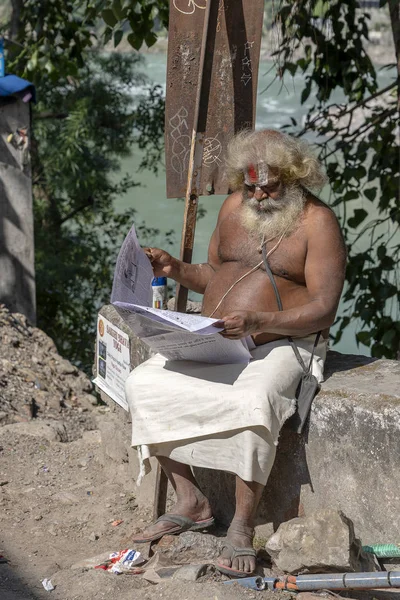 Portrait of Hindu sadhu holy man, sits on the ghat and reads the newspaper on a sunny day near the Ganges river in Rishikesh, India, close up — Stock Photo, Image