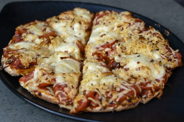 Homemade pizza on a black plate, close up — Stock Photo, Image
