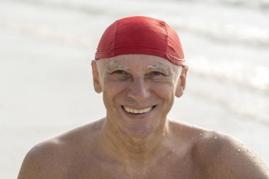 Deniz suyu yakınındaki sahilde kırmızı yüzme şapkalı yaşlı adam