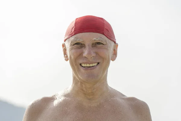 Oudere man in een rode zwemmen hoed op het strand in de buurt van het zeewater — Stockfoto