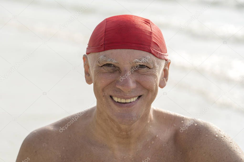 Elderly man in a red swimming hat on the beach near the sea water