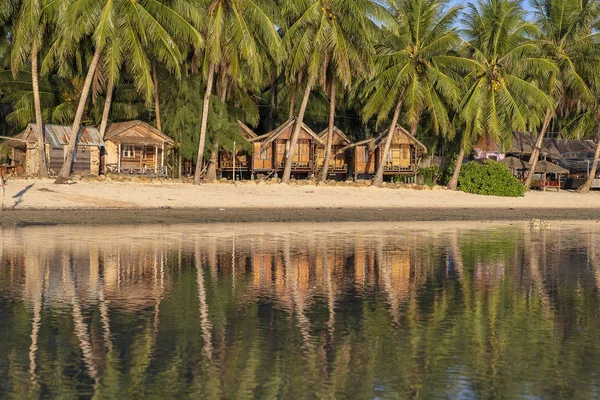 Vacker vik med kokospalmer och träbungalower som återspeglas i havsvatten. Tropisk sandstrand, grönt palmblad och havsvatten på ön Koh Phangan, Thailand — Stockfoto