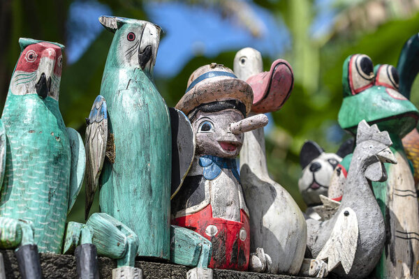 Старые деревянные сувенирные игрушки на каменном заборе возле кукольного магазина в Убуде, остров Бали, Индонезия. Крупный план
