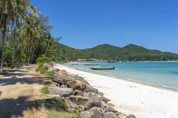 Baía bonita com estrada de terra, água do mar azul, coqueiros e barcos. Praia de areia tropical e água do mar na ilha Koh Phangan, Tailândia — Fotografia de Stock