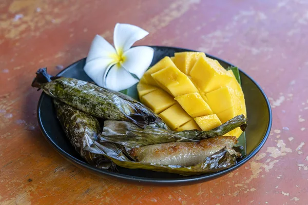 Postre de estilo tailandés, mango amarillo con arroz pegajoso de plátano en hojas de palma. Mango amarillo y arroz pegajoso es popular postre tradicional de Tailandia . —  Fotos de Stock