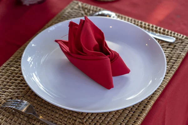 Elegant table setting with fork, spoon, white plate and red napkin in restaurant . Nice dining table set with arranged silverware and napkins