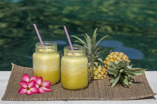 Hemlagad mango och ananas smoothie gjord med kokosmjölk i två glas mugg nära poolen. Ön Bali, Indonesien. Uppfriskande tropisk fruktdryck — Stockfoto