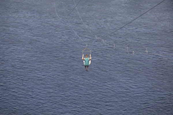 Rückansicht einer jungen Frau, die auf einer Seilrutsche vor dem Hintergrund einer blauen Flusswelle reitet, kyiv, Ukraine — Stockfoto