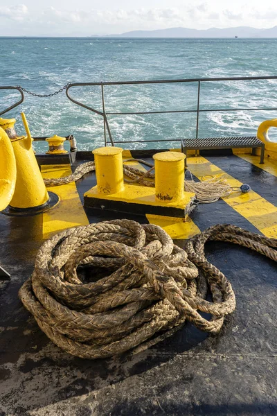 The deck of the ferry boat along with the a thick mooring rope and blue sea water wave, Thailand. Close up