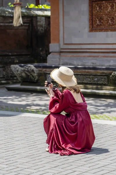 Een meisje in een stro hoed gefotografeerd op de telefoon architectuur in de stad Ubud, eiland Bali, Indonesië — Stockfoto